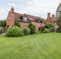 A brick house with dormer windows surrounded by bushes and a lawn with outdoor chairs at Lawn Farm Cottage in Churcham near Gloucester
