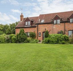 A brick cottage with dormer windows surrounded by bushes and a green lawn at Lawn Farm Cottage in Churcham near Gloucester