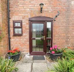 A front door with glass panels set in a brick wall with two small windows and potted plants on either side at Lawn Farm Cottage in Churcham near Gloucester