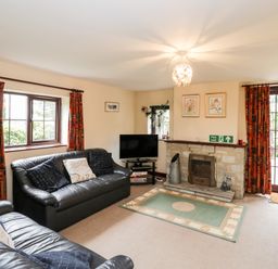 A living room with black leather sofas a fireplace and a television at Lawn Farm Cottage in Churcham near Gloucester