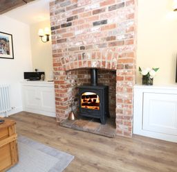 A living room with a wood-burning stove in a brick fireplace flanked by white cabinets at Captains Cottage in Sheringham