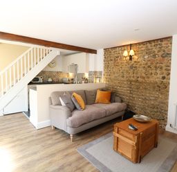 A living room with a sofa and coffee table next to a small kitchen and staircase at Captains Cottage in Sheringham