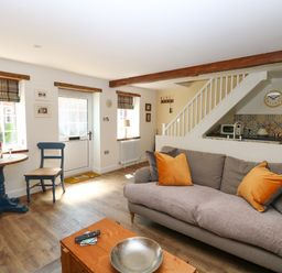 A living room with a sofa and orange cushions a wooden coffee table and a small dining table with chairs at Captain's Cottage in Sheringham