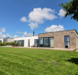 A modern house with a large lawn and patio furniture under a blue sky at Atlantic View in Germoe