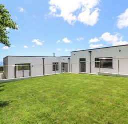 A modern white house with flat roof and large windows behind a lawn and metal railing at Atlantic View in Germoe