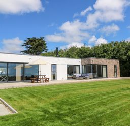 A modern single-story house with large glass windows a patio table with umbrella outdoor seating area and a lawn at Atlantic View in Germoe
