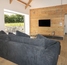 A living room with a black sofa a wall-mounted television wooden paneling and an open door to a kitchen with a silver refrigerator at The Corn Store in St Stephen