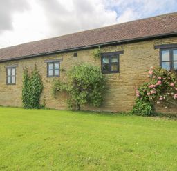 Exterior view of a stone building with black framed windows and climbing plants on a lawn at The Onibury in Craven Arms