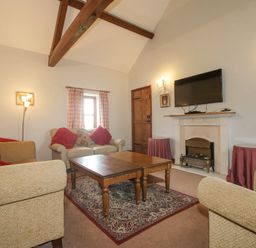 A living room with beige sofas red cushions wooden coffee table and a wall mounted tv at The Onibury in Craven Arms