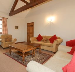 A living room with beige sofas red cushions a wooden coffee table and a window with checked curtains at The Onibury in Craven Arms