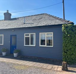A blue exterior wall of a house with three white framed windows and a blue door with two potted plants by the entrance at Stable Cottage in Triscombe