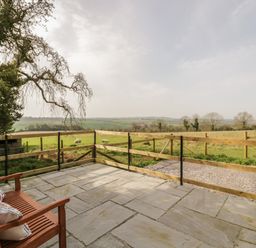A stone patio with a wooden bench and a railing overlooking a grassy field with sheep at The Wash House in Sibford Ferris