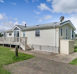 A white modular home with a porch and steps on a grassy plot at Links Lodge in Flookburgh