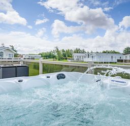 A hot tub with water jets on a deck overlooking mobile homes and grassy area at Links Lodge in Flookburgh