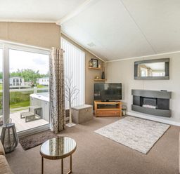 A living room with a television mirror and fireplace by sliding glass doors at Links Lodge in Flookburgh