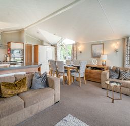 A living room and dining area with brown sofas a wooden dining table with chairs and a kitchen with appliances at Links Lodge in Flookburgh
