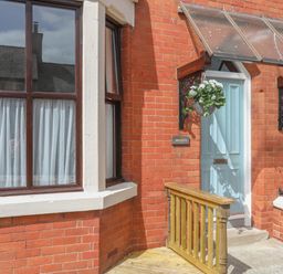 Brick exterior of a house with a blue door, a yellow door, a wooden railing, and a hanging flower basket at Monfa in Cemaes Bay