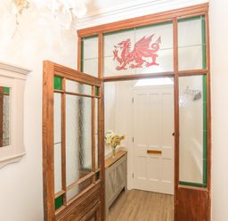 A hallway with a wooden door with textured glass a white door a cabinet with flowers and a mirror at Monfa in Cemaes Bay