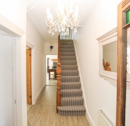 A hallway with striped carpeted stairs a wooden banister a chandelier a wall mirror and doorways leading to other rooms at Monfa in Cemaes Bay
