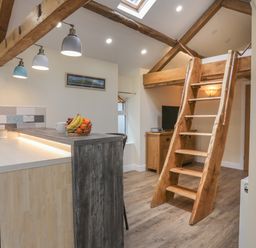 A kitchen area with a wooden counter and fruit bowl next to wooden stairs leading to a loft at Glan Meon Cottage in Barmouth