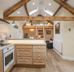 A kitchen area with wooden cabinets and an oven under exposed wooden beams at Glan Meon Cottage in Barmouth