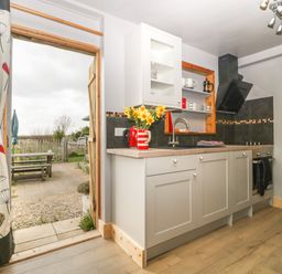 A kitchen with cabinets sink stovetop and open door leading to outdoor seating at Tiny Willow in Farrington near Child Okeford
