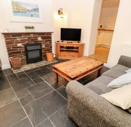 A living room with a gray sofa wooden coffee table stone fireplace and television stand at Bay Tree Cottage in West Looe