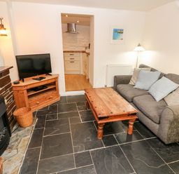 A living room with a gray sofa and wooden coffee table near a brick fireplace and television at Bay Tree Cottage in West Looe