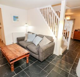 A small living area with a gray sofa and wooden coffee table near white stairs and wooden furniture at Bay Tree Cottage in West Looe