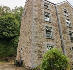 A stone building with multiple windows and outdoor chairs on a patio next to greenery at The Old Mill in Neyland near Milford Haven