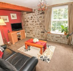 A living room with two black leather sofas a wooden coffee table on a patterned rug a television on a wooden stand a floor lamp and a window with curtains at The Old Mill in Neyland near Milford Haven