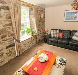 A living room with stone walls a window with curtains a black sofa and a wooden coffee table with flowers at The Old Mill in Neyland near Milford Haven