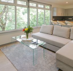 A living room with a beige sofa glass coffee table with flowers and a kitchen with bar stools in the background at The River Lodge in Oban