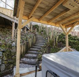 A covered outdoor area with hot tub and wooden stairs leading up a hillside at The River Lodge in Oban