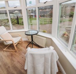 A sitting area with two chairs a small round glass table and large windows showing an outdoor view at The Shieling in Warkworth