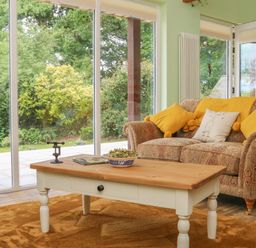 A living room with a patterned sofa with yellow pillows wooden coffee table and large glass doors showing garden at Langdale Barn Sampford Courtenay