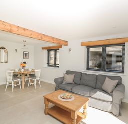A living room with a gray sofa a wooden coffee table and a dining table with white chairs at Kingfisher 2 The Old Stables in Witney