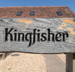 A wooden sign with the word Kingfisher carved into it mounted on a fence outdoors at Kingfisher 2 The Old Stables Witney