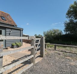 A wooden gate and fence outside a building with a gravel pathway and trees in the background at Kingfisher 2 The Old Stables Witney