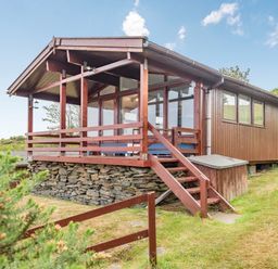A wooden cabin with a stone foundation and a covered porch with railing and stairs surrounded by grass and bushes at The Look Out in Aberdovey