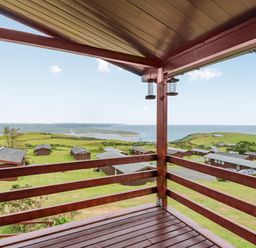A wooden balcony overlooking cabins green fields and a distant coastline at The Look Out in Aberdovey
