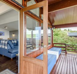 A wooden deck with blue and white bench seats leading to a living room with a blue sofa and dining table at The Look Out in Aberdovey