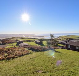 A grassy hillside with several cabins and a view of the sea at The Look Out in Aberdovey