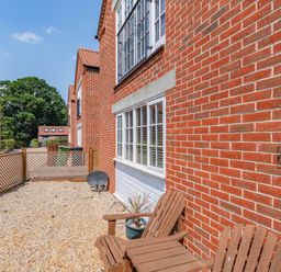 A gravel outdoor area with two wooden chairs and a potted plant outside a red brick house at 26 Burtons Mill in Stalham