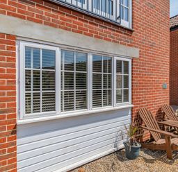 A brick exterior wall with a white framed window wooden chairs and a potted plant at 26 Burtons Mill in Stalham