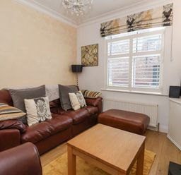 A living room with a brown leather sofa ottoman wooden coffee table window blinds radiator and a television at 202 Salisbury Terrace in York