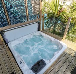 An outdoor hot tub with bubbling water on a wooden deck next to decorative privacy screens and green plants at Daisy Cottage in Benllech