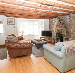 A living room with leather and fabric sofas a stone fireplace a television and a bay window at Arwel in Nefyn