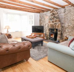 A living room with a stone fireplace a wood stove two sofas a large ottoman and a television at Arwel in Nefyn