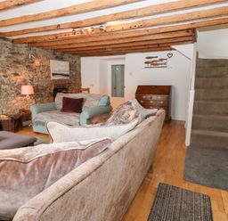 A living room with sofas a lamp and a wooden chest of drawers near carpeted stairs at Arwel in Nefyn